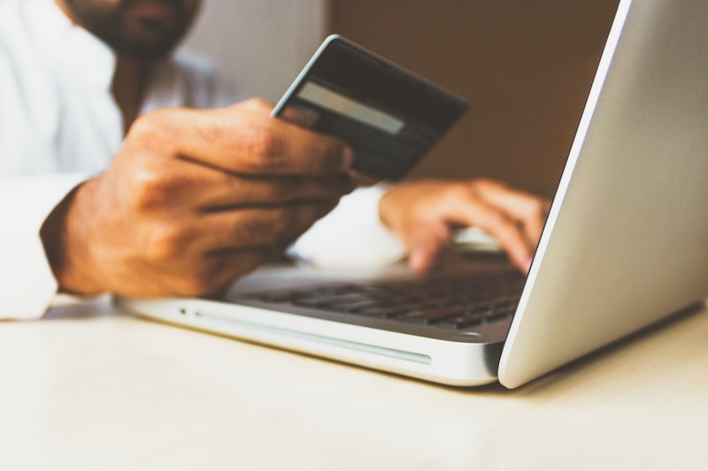 hand holding a credit card near a laptop