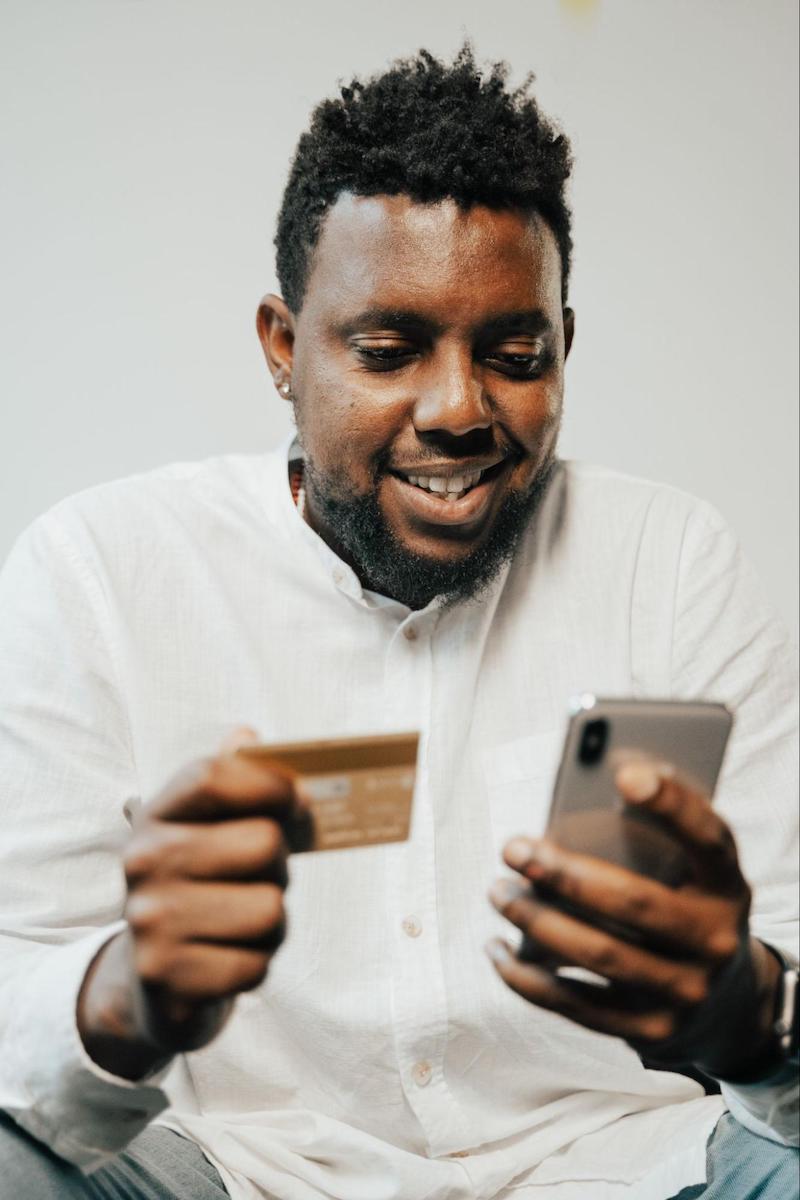 Man excitedly looking at a mobile phone in one had and a credit card in the other